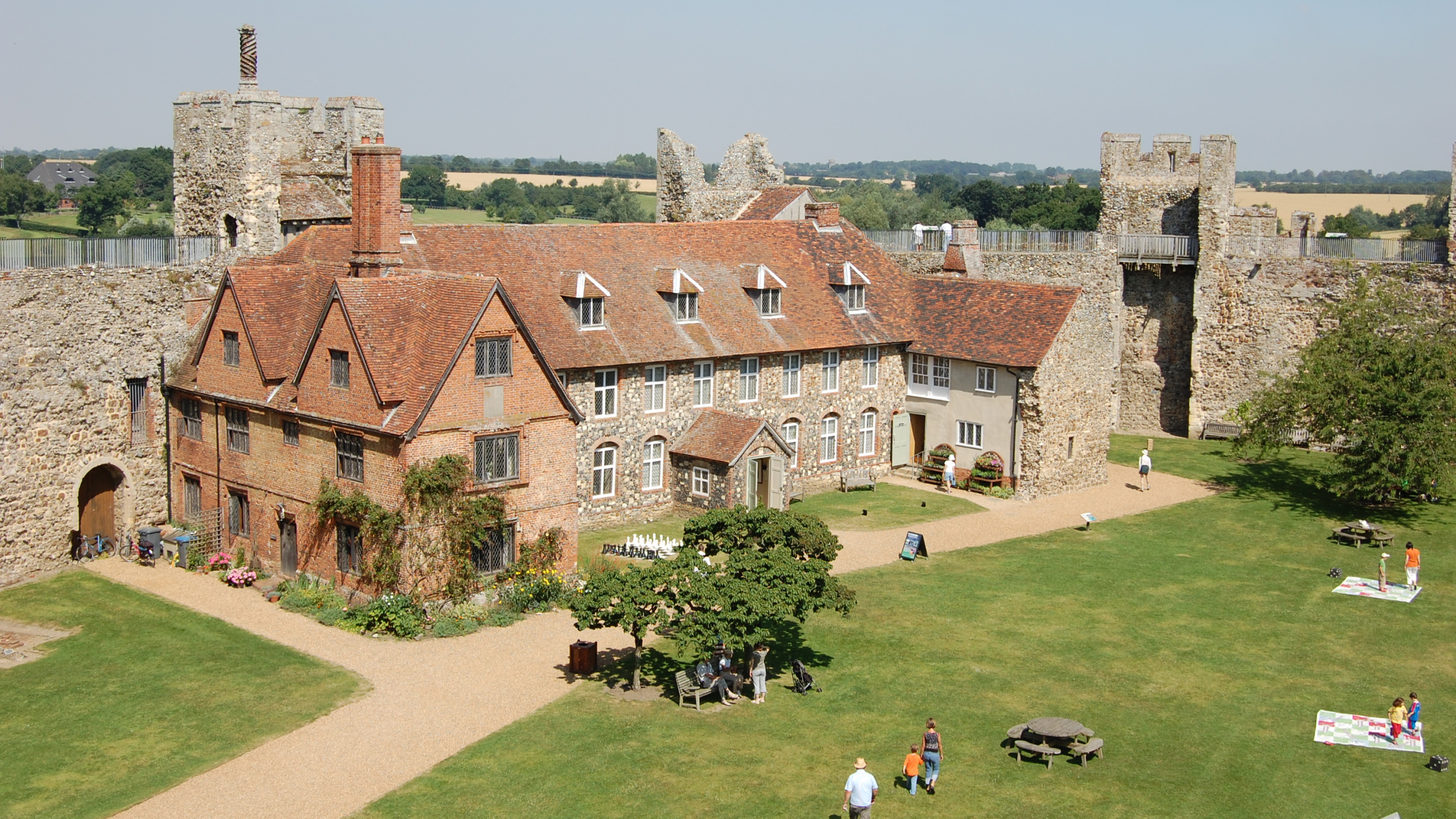 Personnes Marchant Sur un Terrain D'herbe Verte Près D'un Bâtiment en Briques Brunes Pendant la Journée. Wallpaper in 2560x1440 Resolution