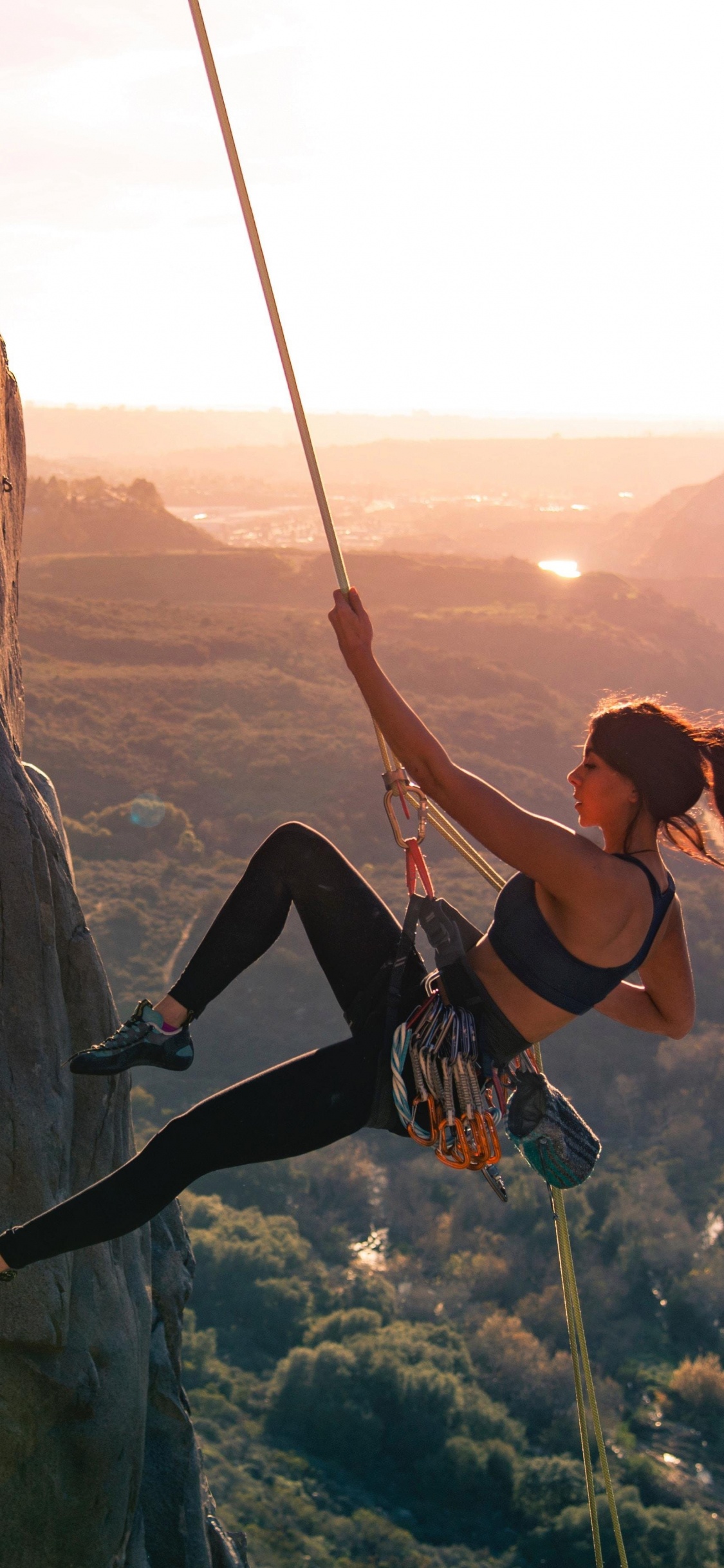 Woman in Black Tank Top and Black Pants Climbing on Brown Rock Formation During Daytime. Wallpaper in 1125x2436 Resolution