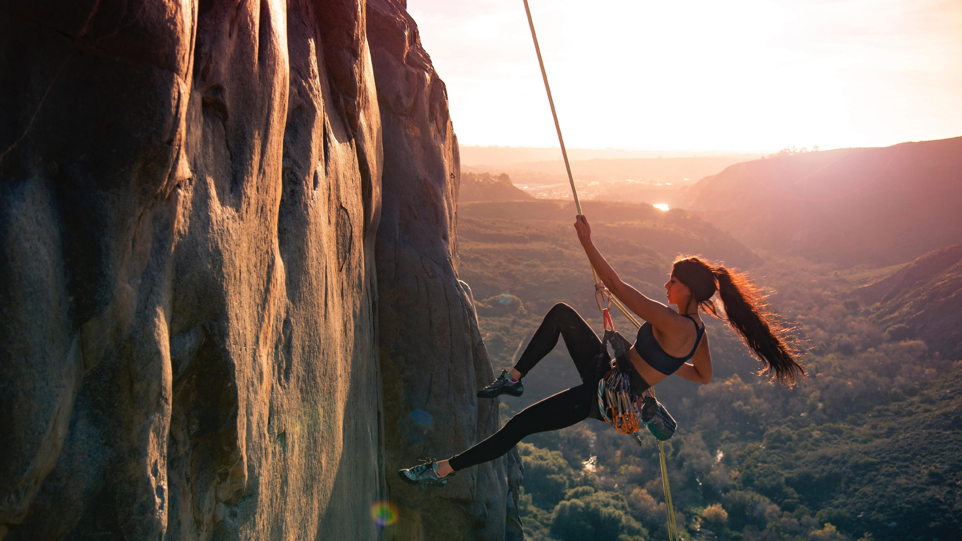 Woman in Black Tank Top and Black Pants Climbing on Brown Rock Formation During Daytime. Wallpaper in 1920x1080 Resolution