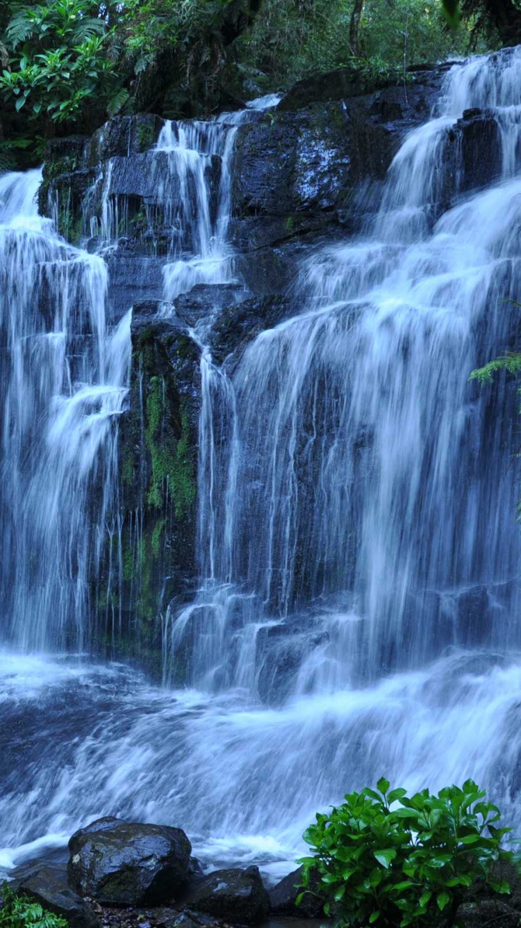 L'eau Tombe au Milieu Des Rochers Couverts de Mousse Verte. Wallpaper in 750x1334 Resolution