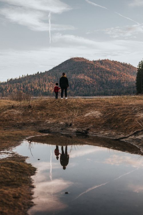 2 person standing on brown grass field near lake during daytime