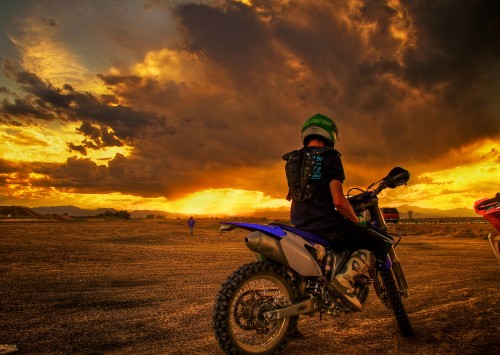 Image man riding motorcycle on brown field during sunset