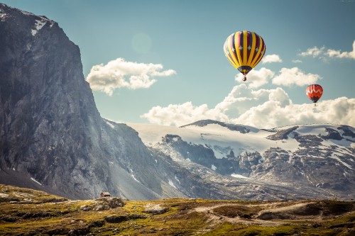 Image yellow and green hot air balloon flying over snow covered mountain during daytime