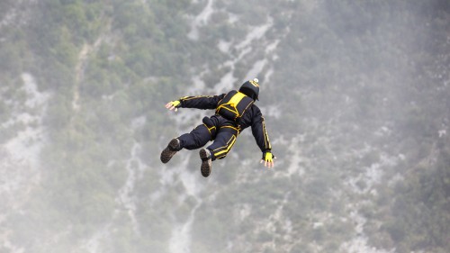 Image man in black and yellow jacket and black pants jumping on mid air under white clouds