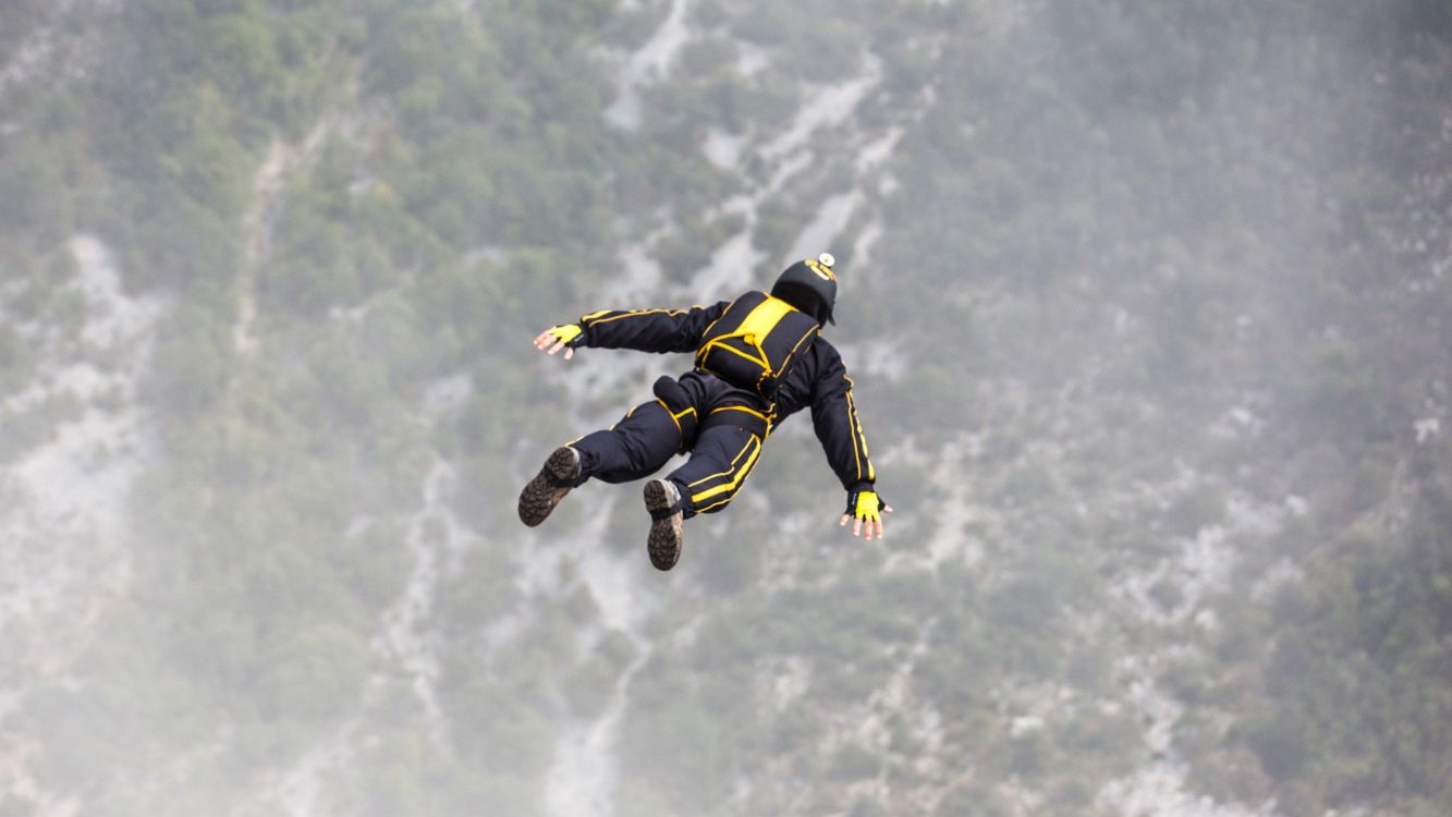 man in black and yellow jacket and black pants jumping on mid air under white clouds