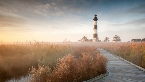 Image white and black lighthouse near brown trees under white clouds during daytime