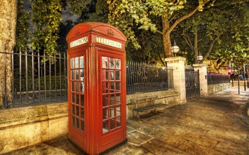 Image red telephone booth near green trees during daytime