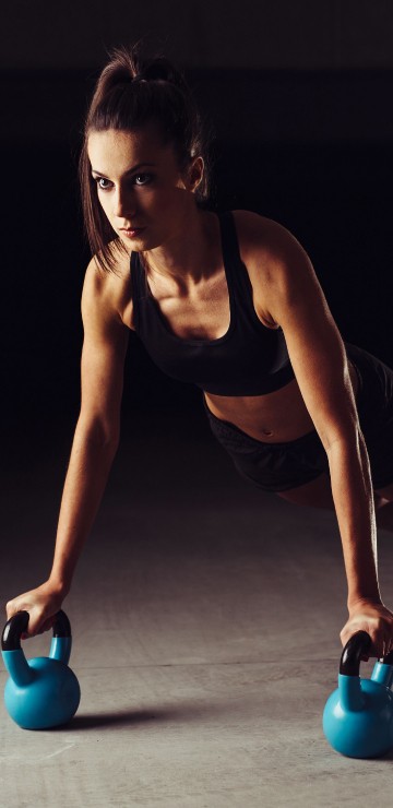 Image woman in black tank top and black pants holding blue kettle bell