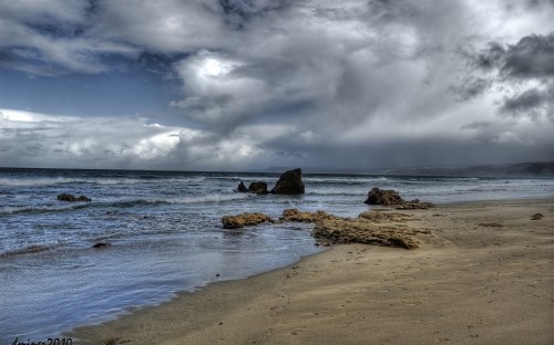 Image brown rock formation on sea shore under white clouds and blue sky during daytime