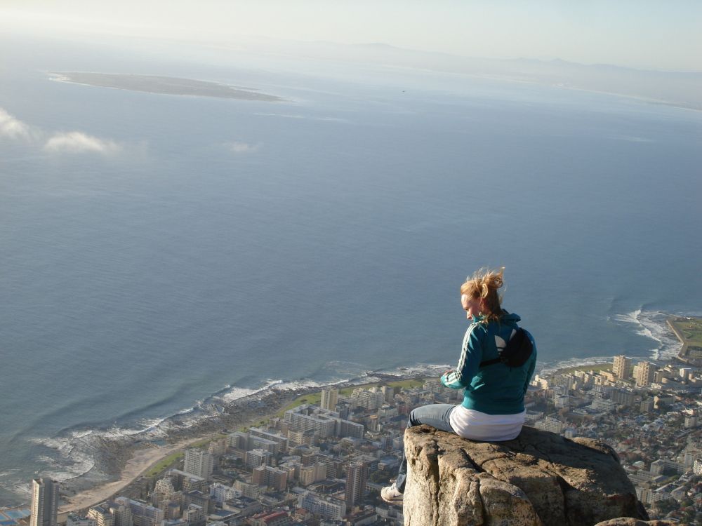 woman in blue long sleeve shirt sitting on rock formation near sea during daytime