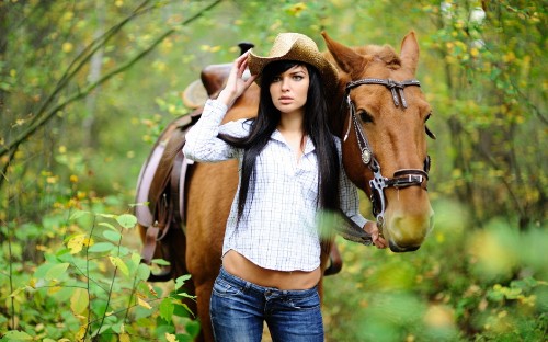 Image woman in white and black striped shirt and blue denim jeans standing beside brown horse during