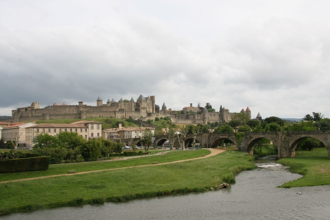 brown concrete building near green grass field and river under white clouds during daytime