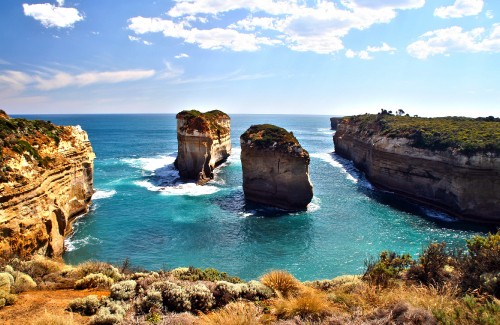 Image brown and green rock formation on blue sea under blue and white cloudy sky during daytime