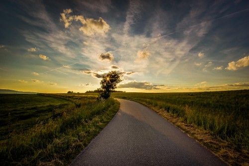 Image gray asphalt road between green grass field under blue and white sunny cloudy sky during daytime