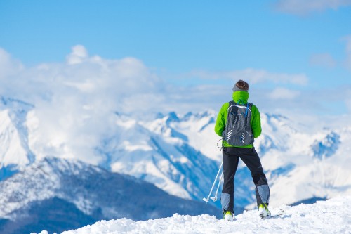 Image man in green jacket and black pants standing on snow covered ground during daytime