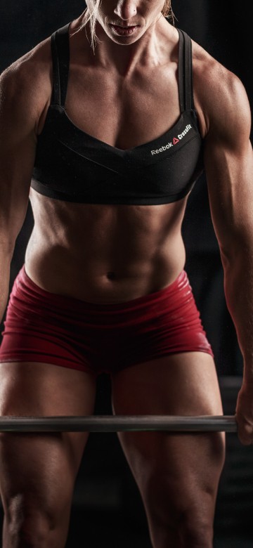 Image woman in black sports bra and red shorts holding black barbell