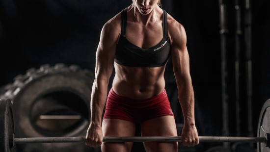 Image woman in black sports bra and red shorts holding black barbell