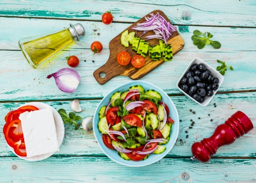 Image sliced vegetables on white ceramic bowl beside brown wooden chopping board