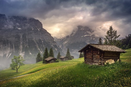 Image brown wooden house on green grass field near mountain under white clouds during daytime