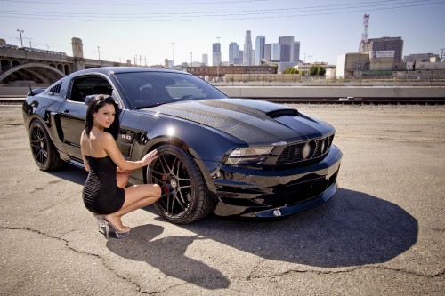 Image woman in black tank top and black shorts leaning on black car