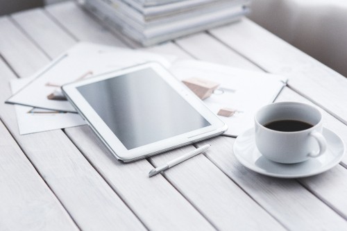 Image white ipad on white book page beside white ceramic mug on table