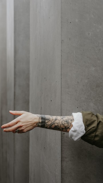 Image person in brown jacket with black tattoo on left hand