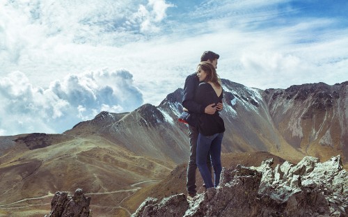 Image man in black jacket and black pants standing on rock formation under white clouds during daytime