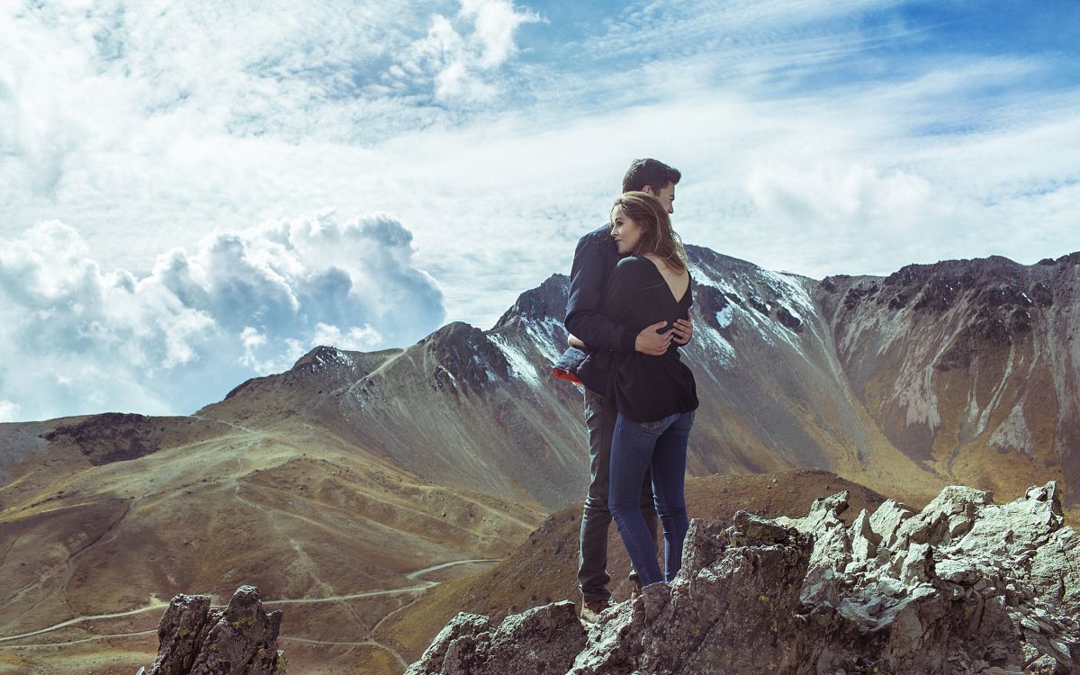 man in black jacket and black pants standing on rock formation under white clouds during daytime