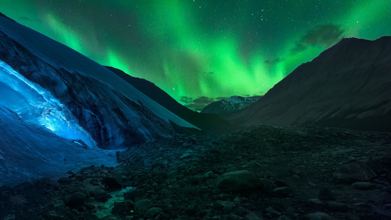 green aurora lights over snow covered mountain