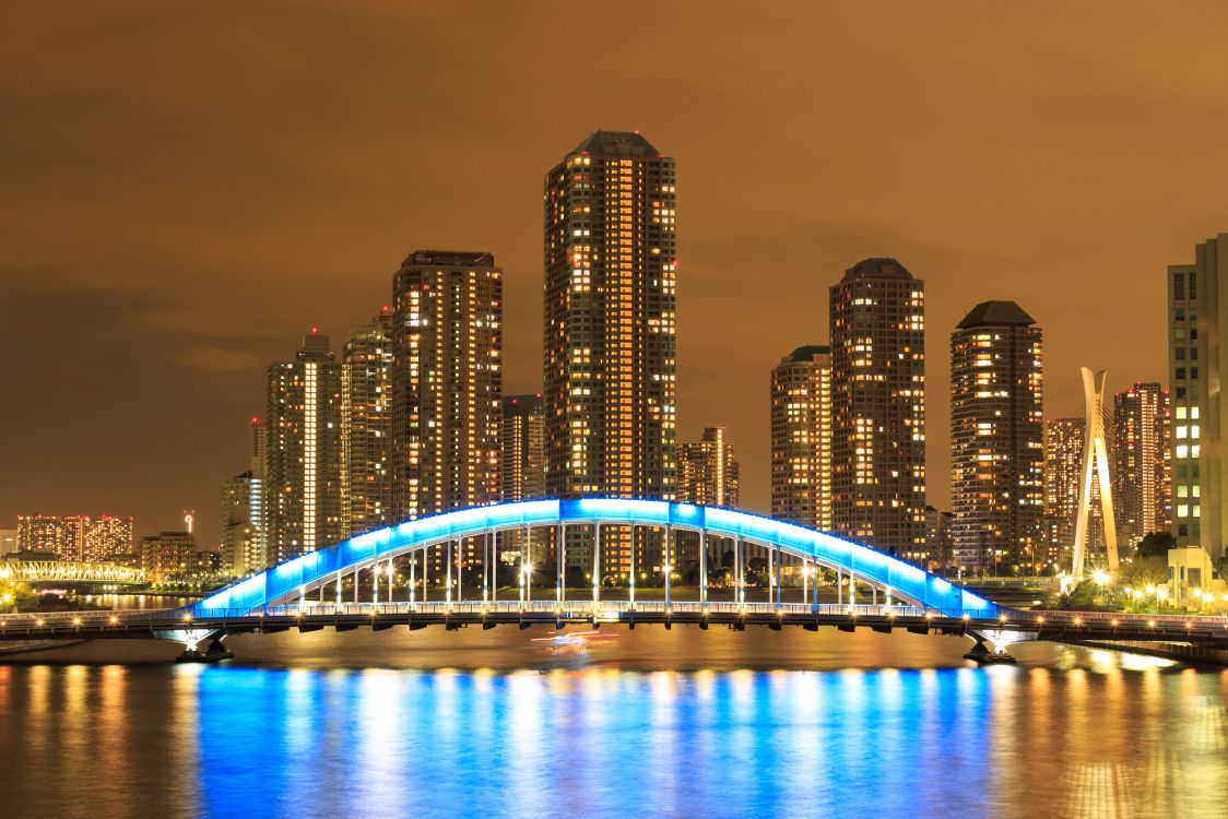 Puente Iluminado Sobre el Cuerpo de Agua Cerca de Los Edificios de la Ciudad Durante la Noche. Wallpaper in 7000x4667 Resolution