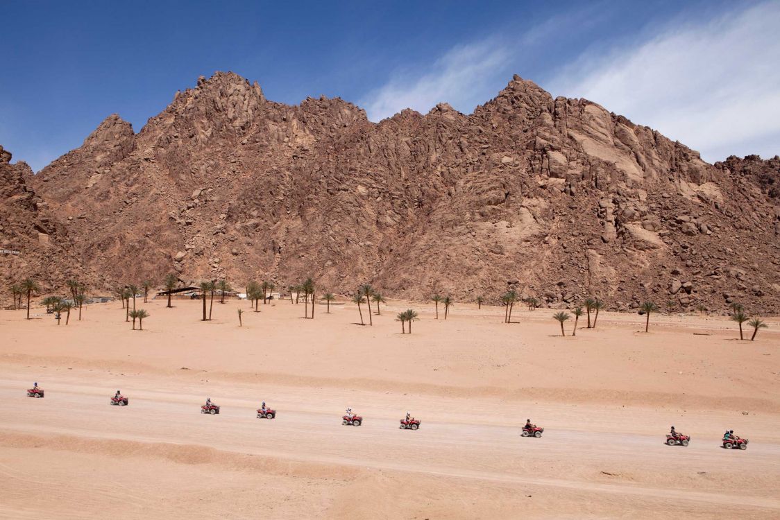 people walking on beach near brown rocky mountain during daytime