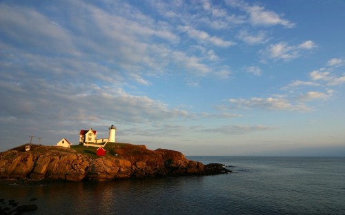 Image white lighthouse on brown rock formation near body of water during daytime