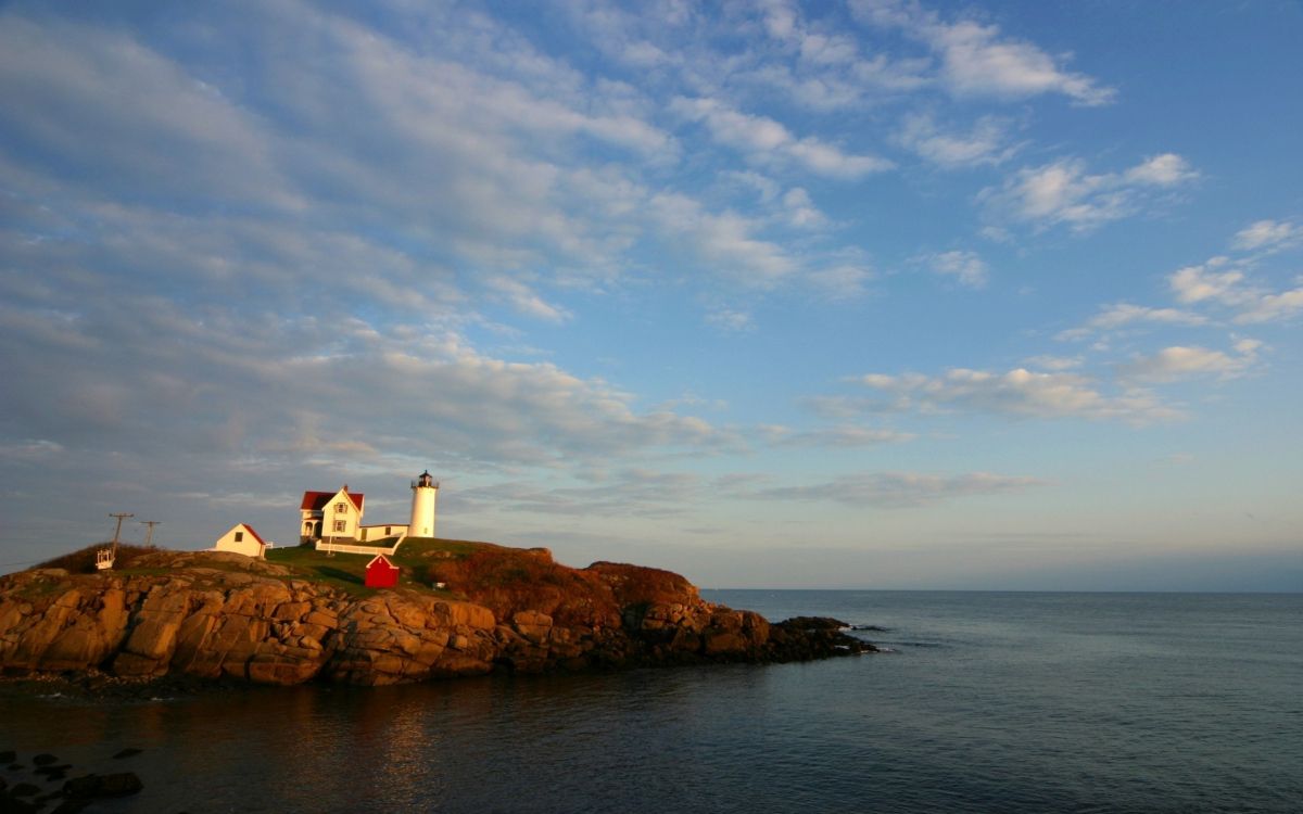 white lighthouse on brown rock formation near body of water during daytime