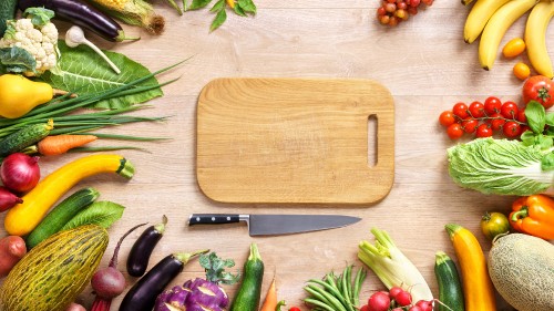 Image brown wooden chopping board beside green and purple vegetables