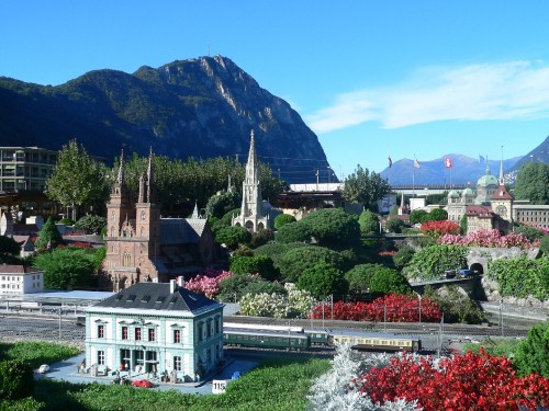 Image white and brown concrete building near green trees and mountain under blue sky during daytime