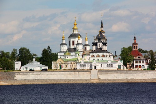 Image white and gold concrete building near green trees under white clouds during daytime