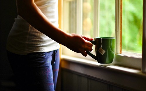 Image person in white shirt and blue denim jeans holding green ceramic mug