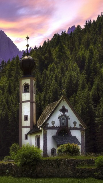 Image white and black church on green grass field near green trees and mountains during daytime