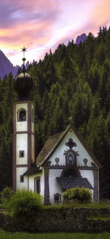 Image white and black church on green grass field near green trees and mountains during daytime