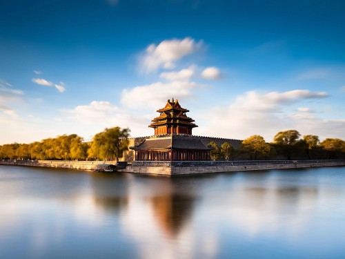 Image brown and black concrete building near body of water under blue sky during daytime