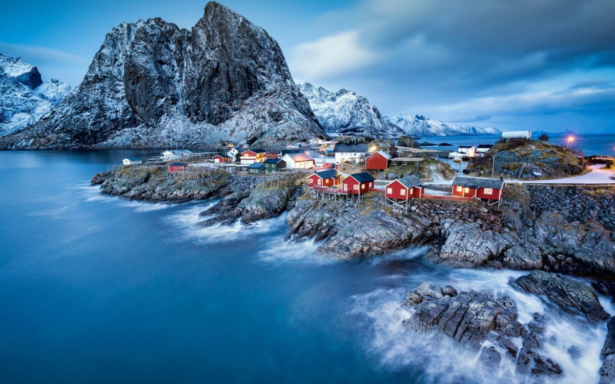 houses near rocky mountain and body of water during daytime