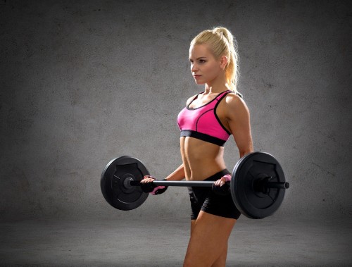 Image girl in pink sports bra and pink shorts holding black dumbbell