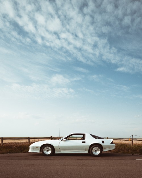 Image white coupe on brown field under white clouds during daytime