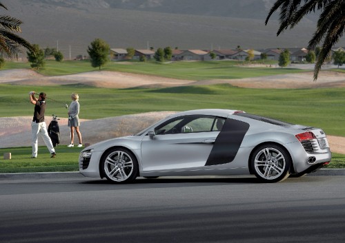 Image man in white t-shirt and white shorts standing beside silver porsche 911 coupe during daytime