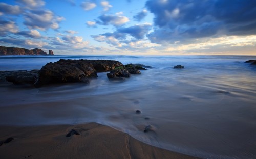 Image brown rock formation on sea shore under blue sky and white clouds during daytime