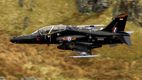 Image black and yellow fighter jet flying over green trees during daytime