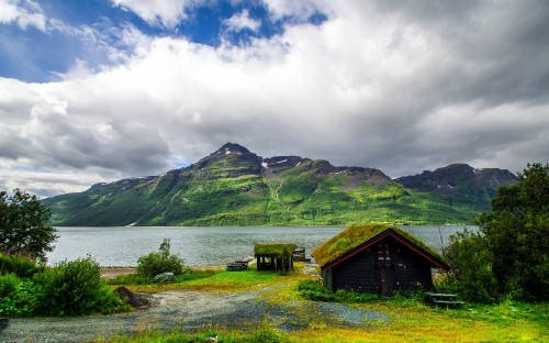 Image brown wooden house on green grass field near lake under white clouds and blue sky during