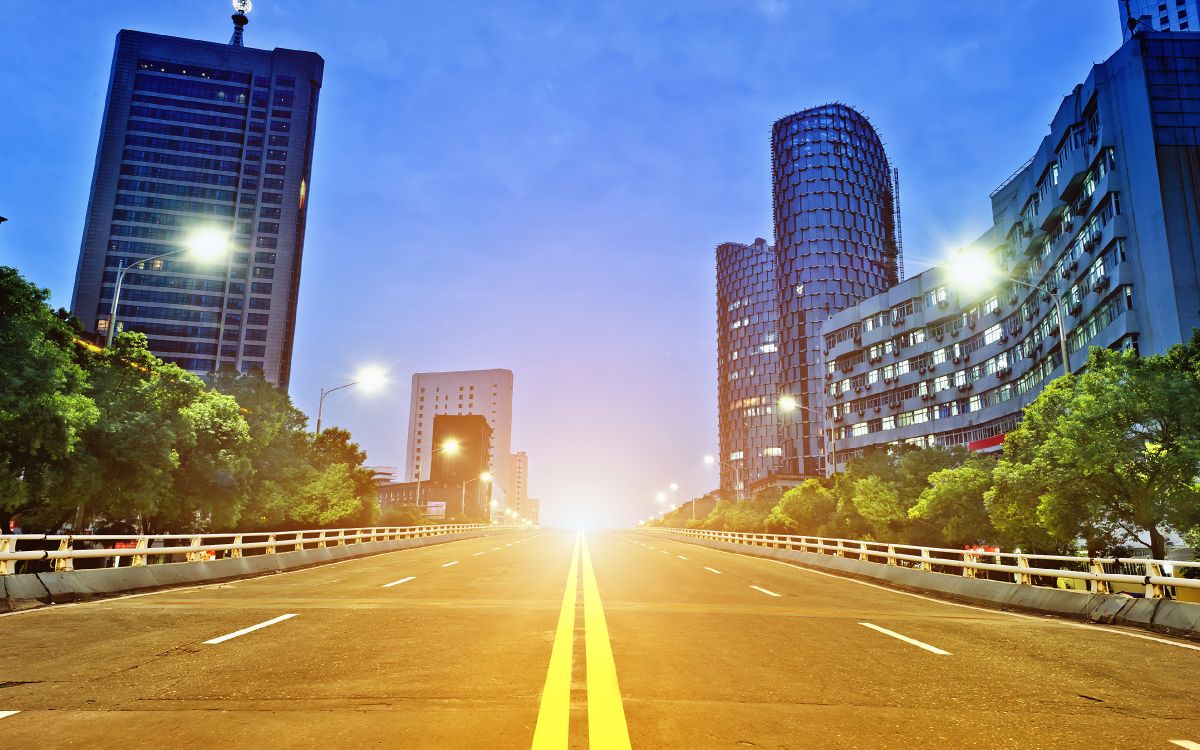 gray concrete road between green trees and high rise buildings during daytime