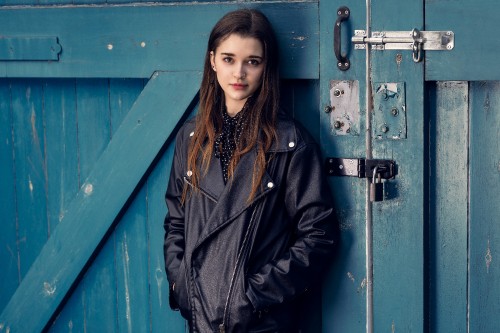 Image woman in black coat standing beside blue wooden door