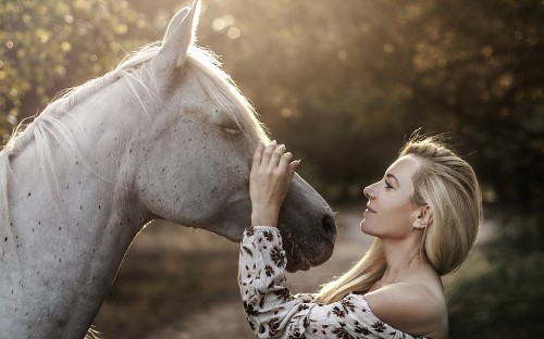 Image woman in black and white floral shirt beside white horse during daytime